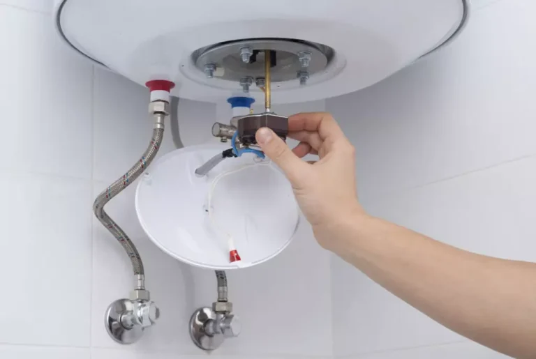 Electrician connecting hot and cold water inlet pipes under a storage water heater during installation in Singapore