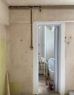 Bathroom wall with pipes and wiring prepared for water heater installation in Singapore